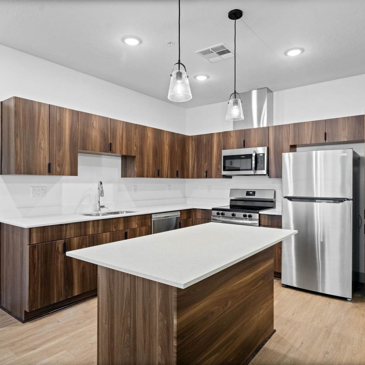 Modern kitchen with wood cabinets, stainless steel appliances, white countertops, and pendant lighting.