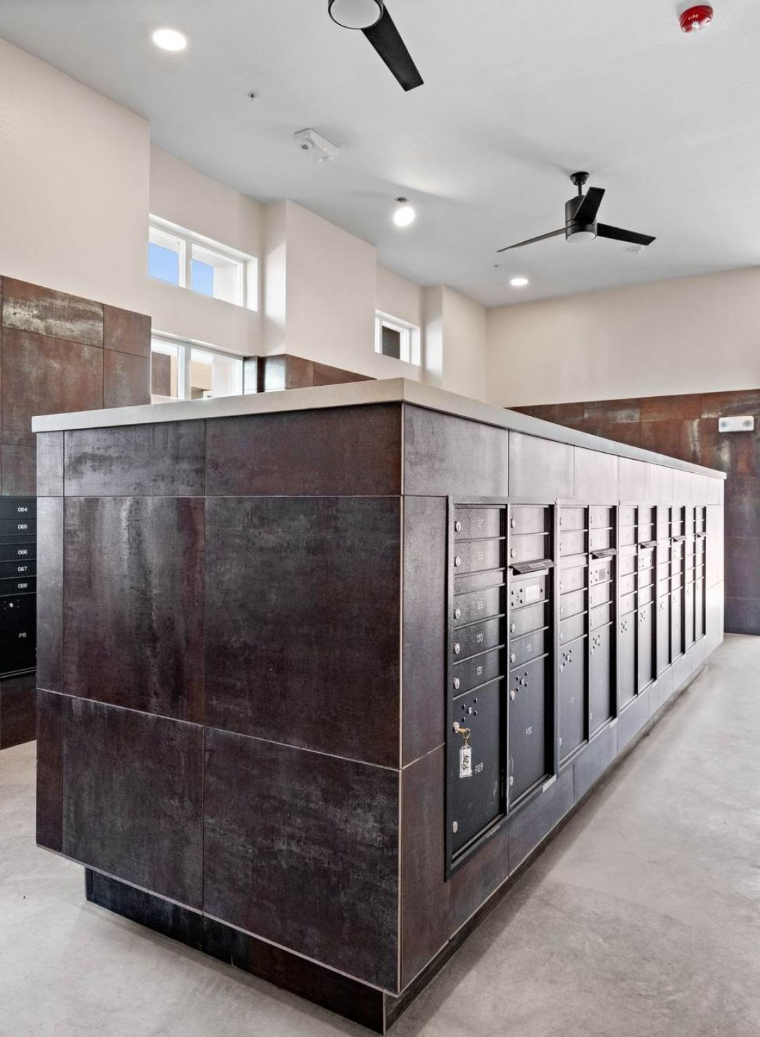 Modern package and mail room with brown lockers, large windows, and a ceiling fan.