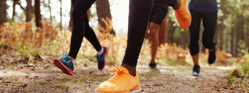 Four people running on a forest trail, focusing on bright orange running shoes in the foreground.