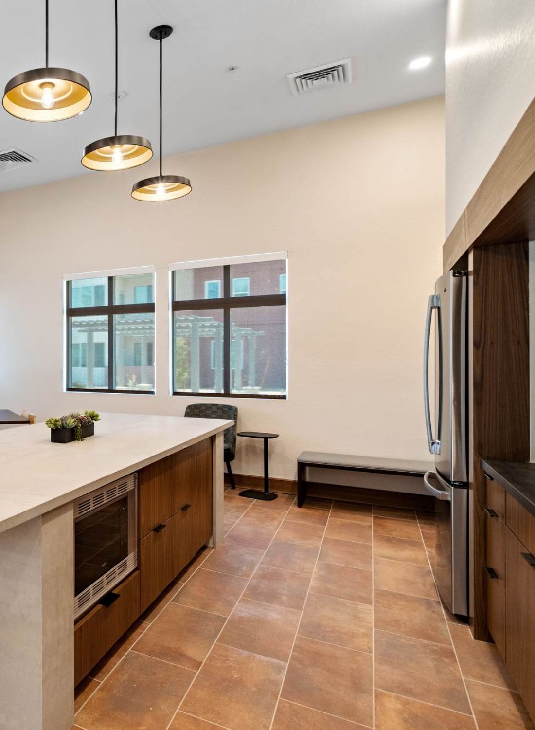 Modern communal kitchen with island, wooden chairs, large windows, and pendant lights.