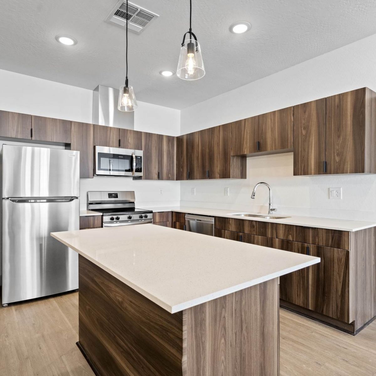 Modern kitchen with wood cabinets, stainless steel appliances, island, and pendant lights.