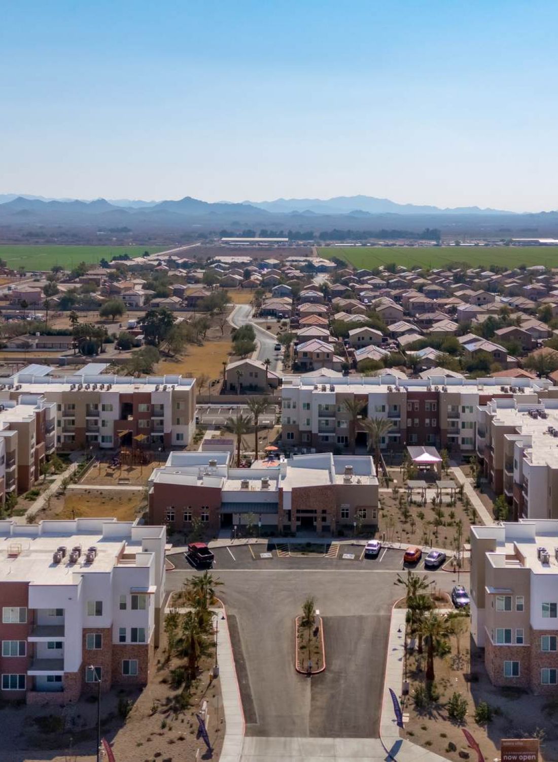 Aerial view of modern apartment buildings with suburban houses and mountains in the distance under a clear sky.