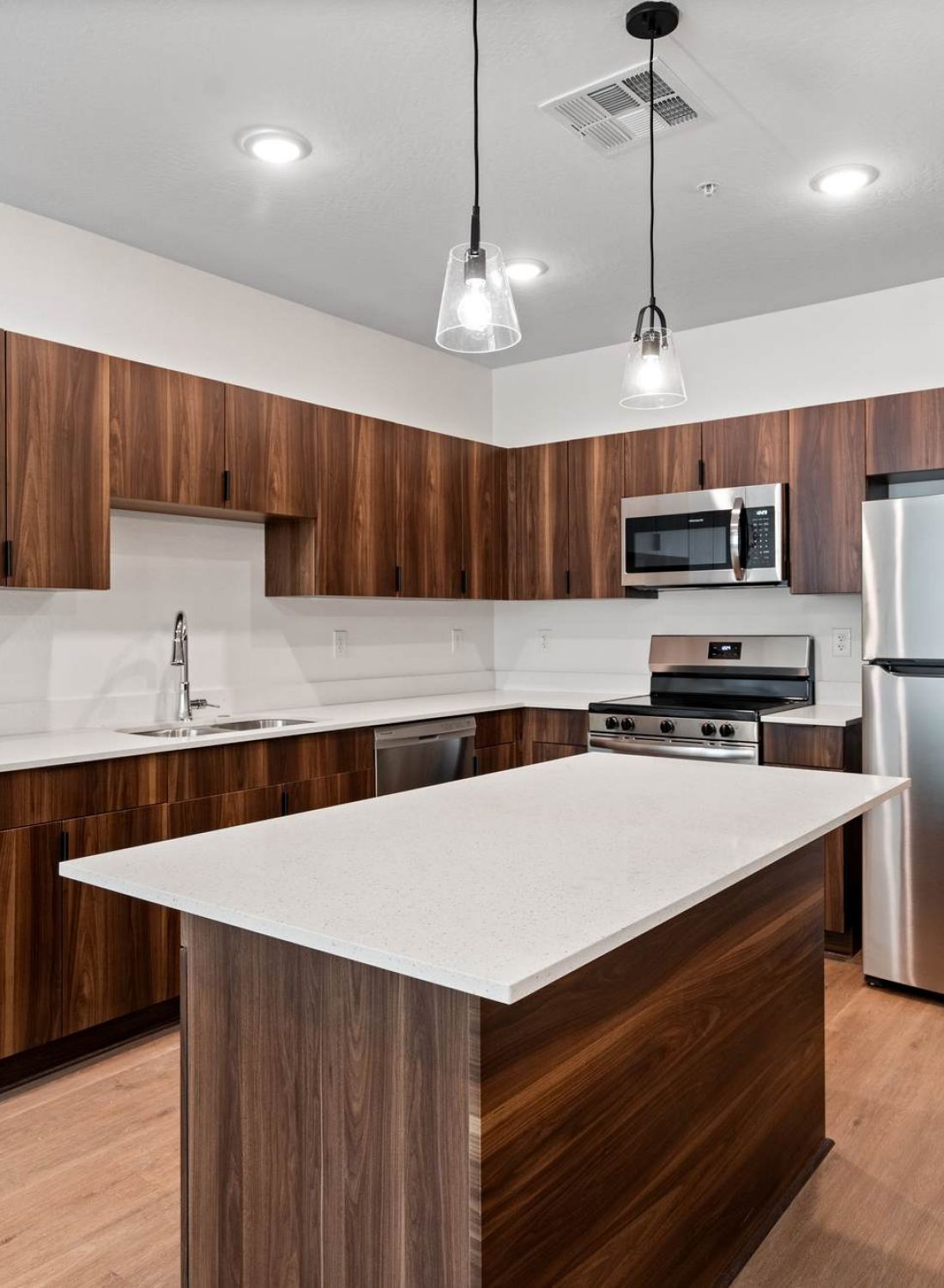 Modern kitchen with wood cabinets, stainless steel appliances, an island, and pendant lighting.