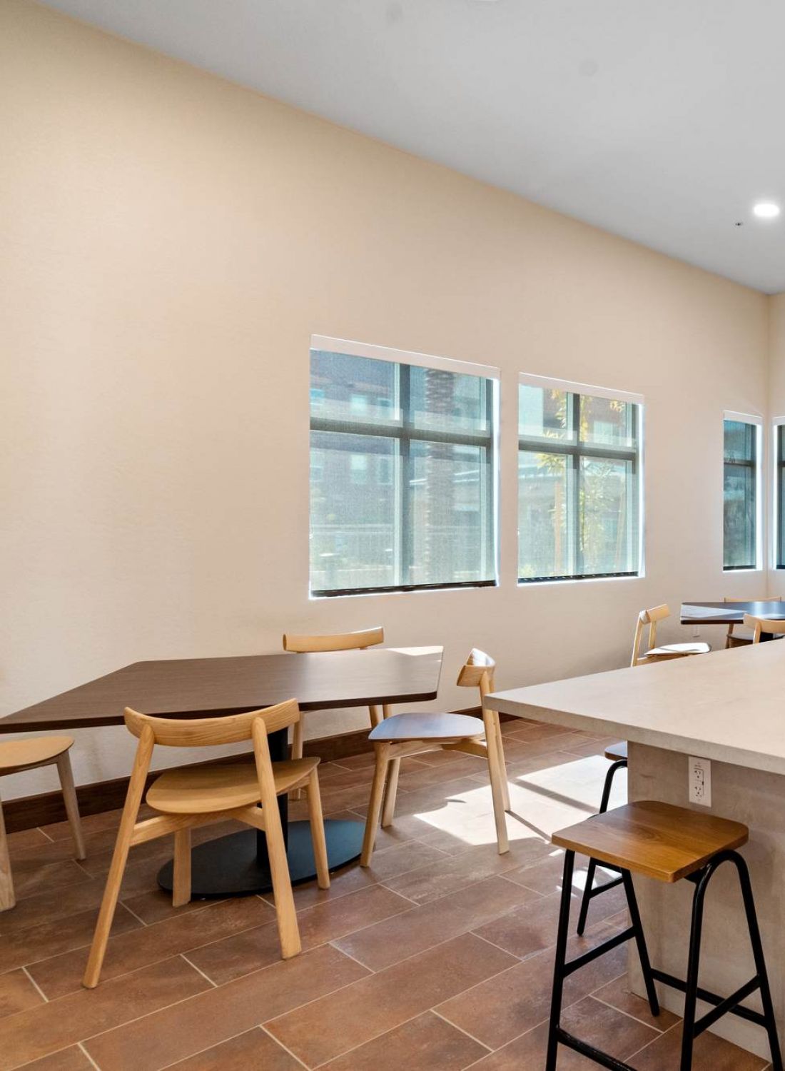 Modern communal kitchen with island, wooden chairs, large windows, and pendant lights.