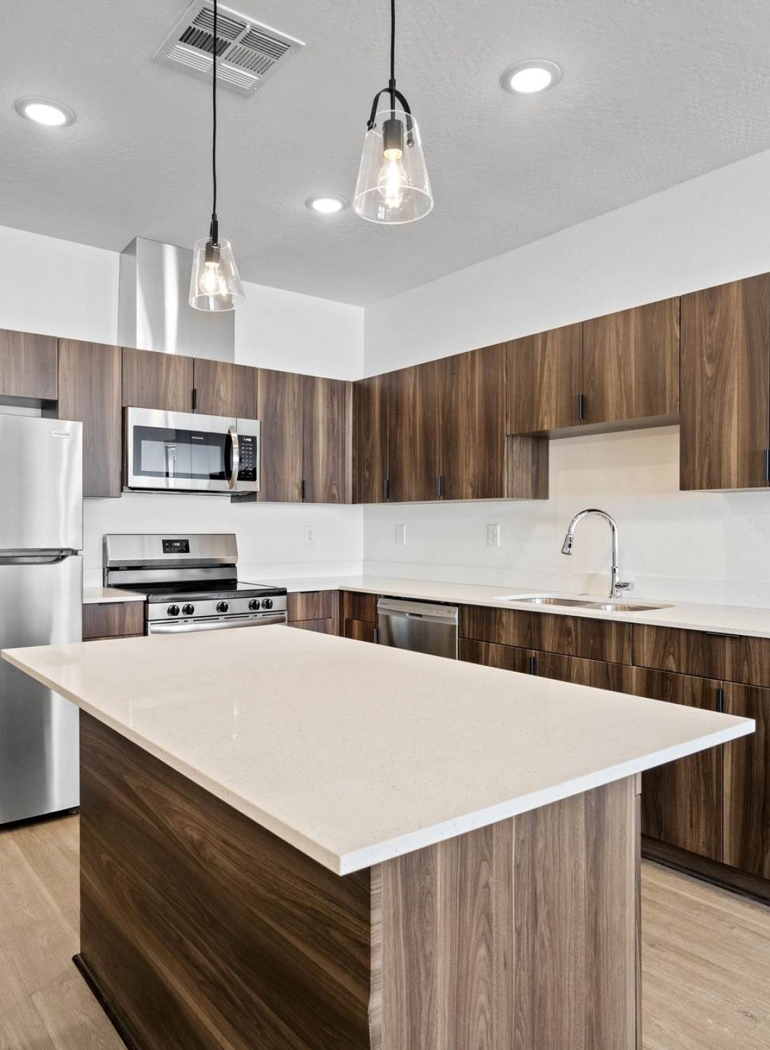 Modern kitchen with wood cabinets, stainless steel appliances, island, and pendant lights.