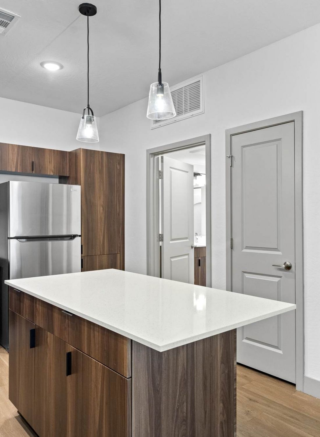 Modern kitchen with wood cabinets, stainless steel appliances, and stacked washer and dryer in an open closet.
