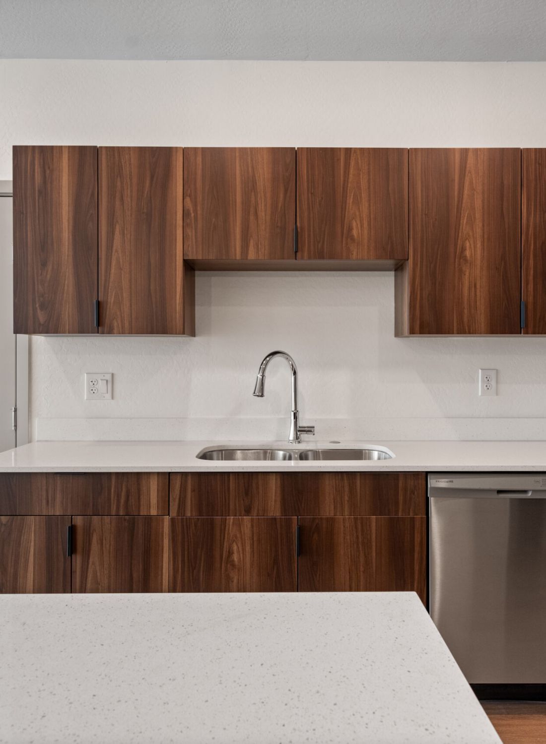 Modern kitchen with wood cabinets, white countertops, stainless steel sink, and built-in dishwasher.